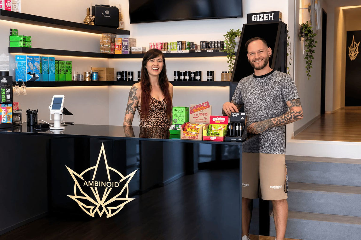 Two smiling staff members behind the Ambinoid counter, shelves of CBD and vape products in the background.